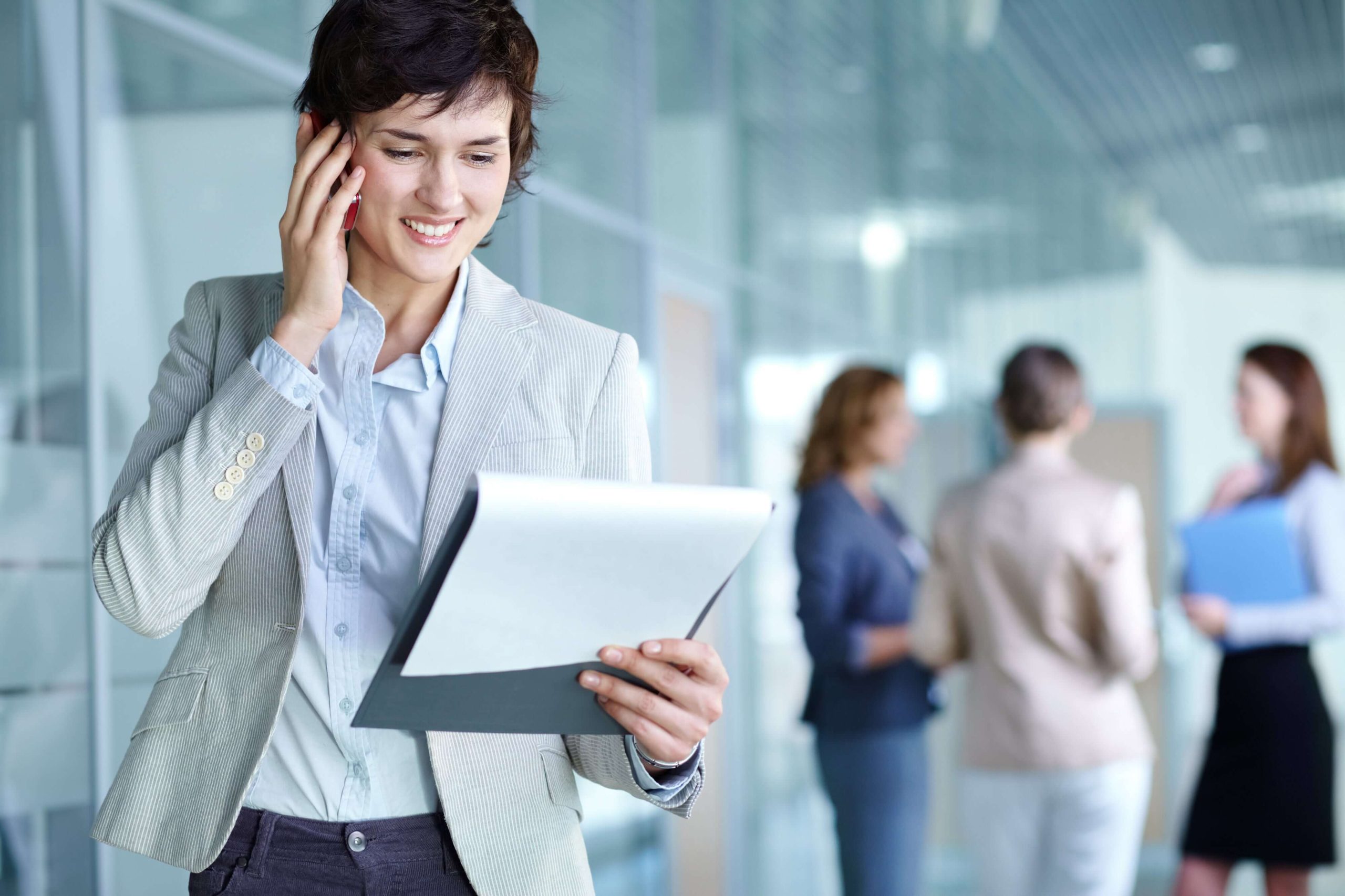 image-of-busy-female-calling-on-the-phone-and-reading-document-in-working-environment-SBI-304869129-min